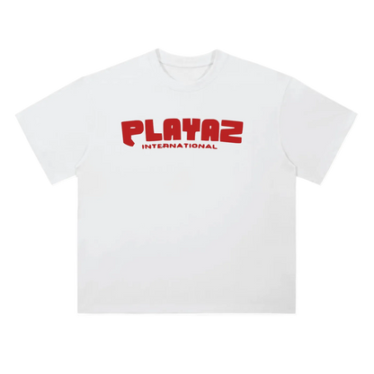 A white short-sleeve crewneck t-shirt featuring a red graphic print on the chest that reads 'PLAYAZ INTERNATIONAL' in a bold, stylized font.