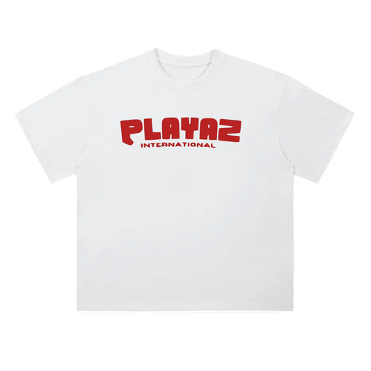 A white short-sleeve crewneck t-shirt featuring a red graphic print on the chest that reads 'PLAYAZ INTERNATIONAL' in a bold, stylized font.