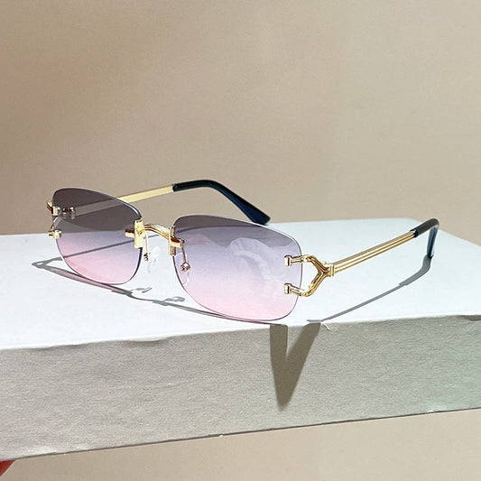 Sunglasses with gold frame and pink gradient lenses on a light gray surface.